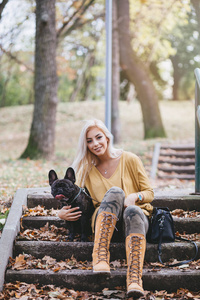 美丽和快乐的女人享受在公园享受与她可爱的法国斗牛犬。秋季时间