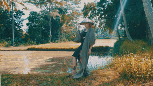 美丽的时尚女孩和服和传统的巴厘岛草帽摆在热带稻田梯田。时尚时髦女性户外肖像