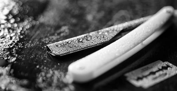 一把危险的剃刀和一把金属刀片放在桌子上.男士剃须照片