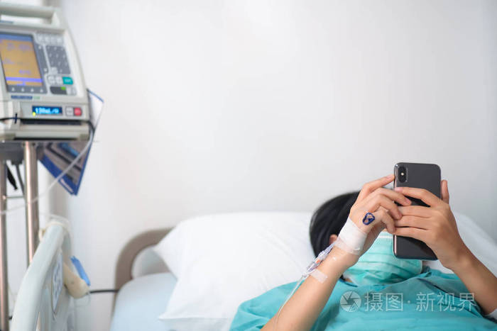 年轻妇女患者躺在床上在医院玩智能手机与静脉正常salin