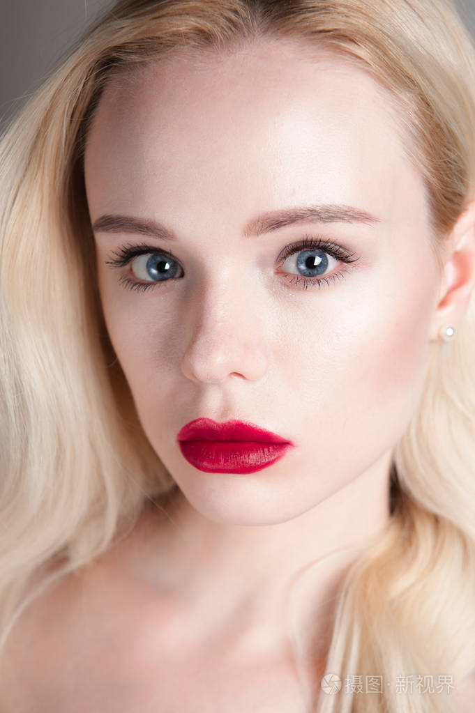 完美的化妆美容模型女孩红红的嘴唇和蓝色的眼睛看着照相机.