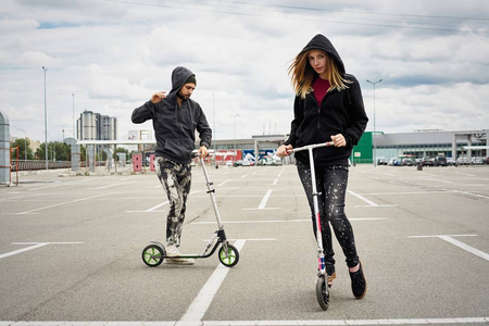 年轻时尚夫妇与踢滑板车在城市背景