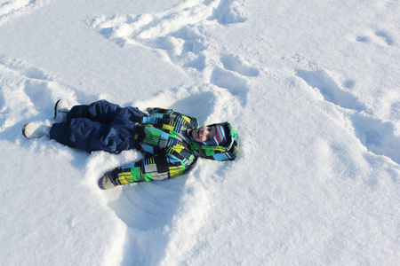 这个小男孩穿着颜色夹克着躺在雪上的微笑