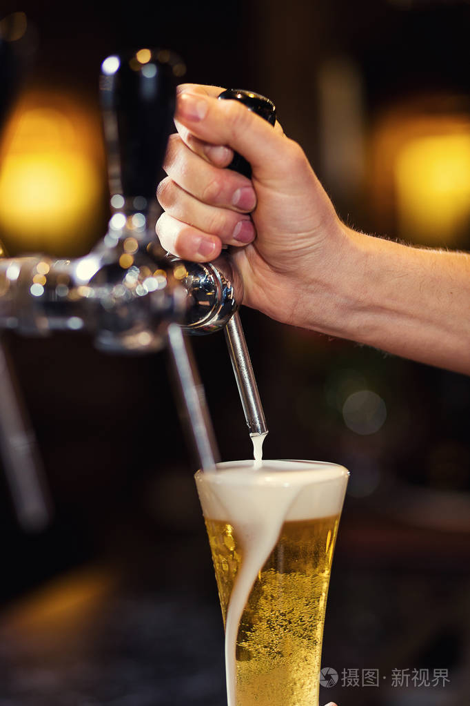 酒保手在浇注吃水的啤酒,啤酒从水龙头 玻璃装满啤酒 鲜啤酒 酒吧的
