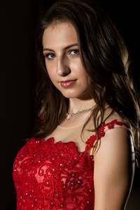 漂亮的年轻女子在黑暗的房间里摆着红色礼服。专业化妆