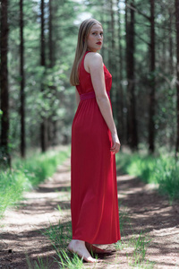穿红色连衣裙的金发女郎在森林小路上看着肩膀