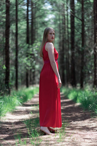 穿红色连衣裙的金发女郎在森林小路上看着肩膀