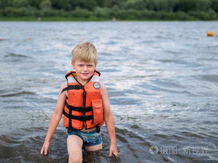 可爱的小男孩在橙色生活背心游泳在河里