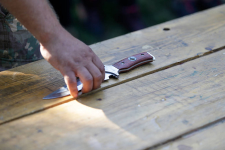 男子手持一把军用刀在一张木桌上照片