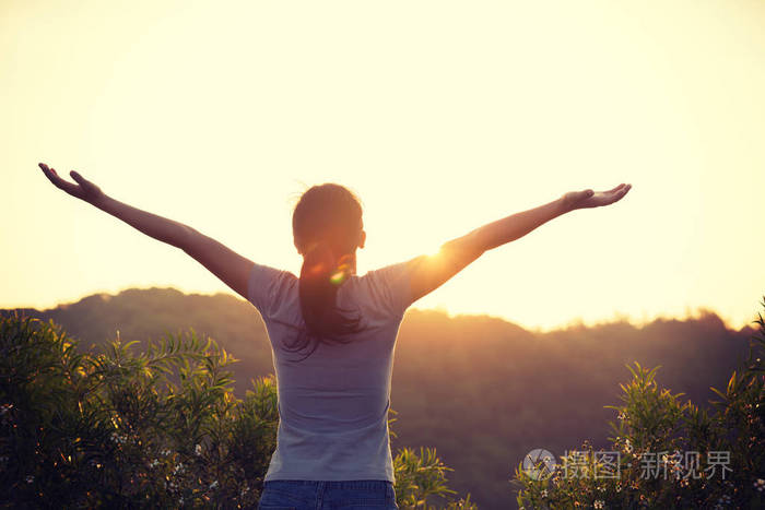 自由妇女举起胳膊到日出在山顶在早晨