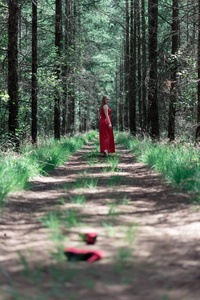 穿红色连衣裙的金发女郎穿着丢失的鞋子走在森林小路上