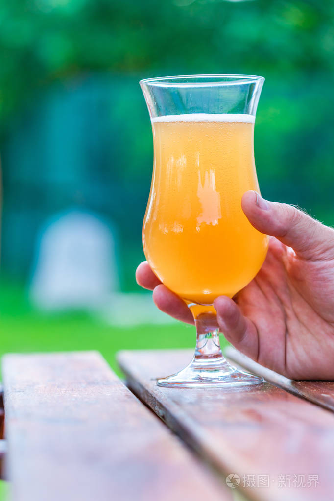 男手捧着一杯冰镇啤酒放在花园的桌子上
