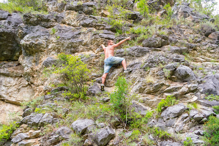 穿着牛仔裤和裸露躯干的年轻人爬上岩石到阿尔泰山的顶端, 没有设备和保险点, 他的手侧