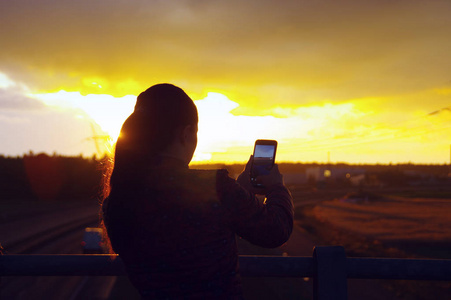 制作日落照片的女孩剪影。年轻女性使用智能手机相机和寻找太阳方向