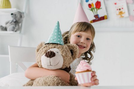 微笑的生日孩子拿着泰迪熊和给蛋糕