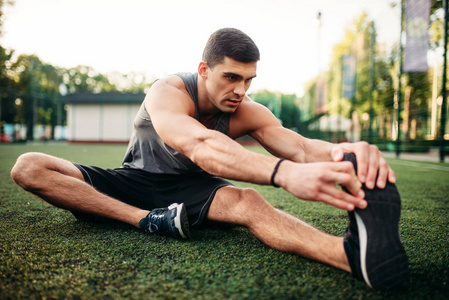 运动员坐在草地上做伸展运动照片