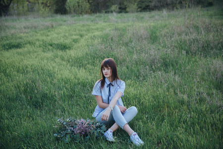 美丽的坐着的女孩与绿色的花束在田野里