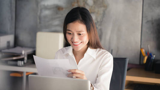 年轻的亚洲商界女性在工作场所微笑, 在办公室读报纸