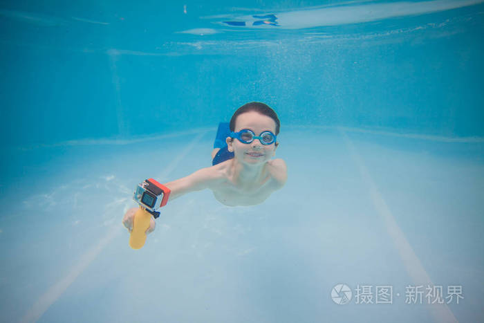 快乐的小宝贝在水池用行动照相机水下游泳。射击在水之下。横向打印