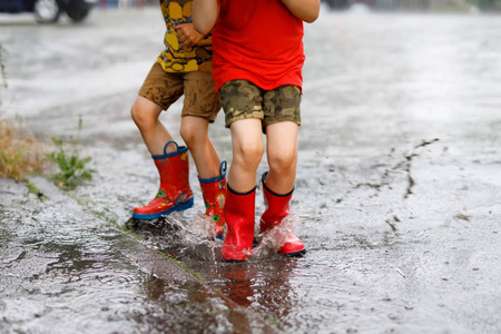 两个孩子穿红色雨鞋跳进了水坑里