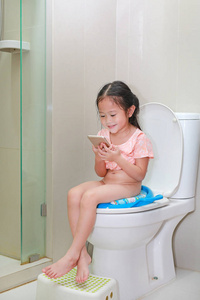 小亚洲女孩坐在厕所和看智能手机一起