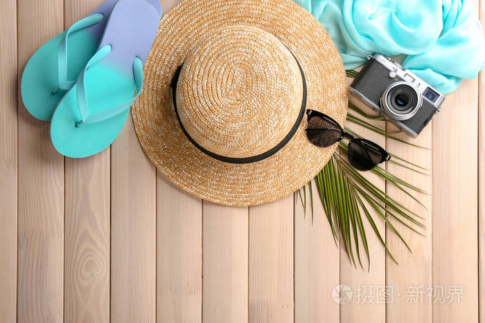 在木质背景下, 带有时髦帽子照相机和沙滩物体的平躺组合物