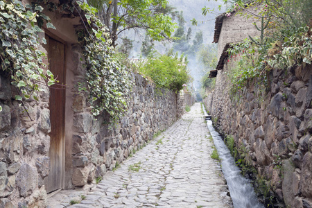 大气狭窄鹅卵石街道与土坯房子, 水渠道奔跑反对墙壁在历史悠久的安第斯镇坦波, 圣洁谷, 秘鲁