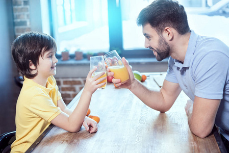 微笑的小男孩和他的父亲无比由杯子与果汁在桌