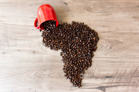 非洲形状的咖啡豆在一个木桌上, 从一个红色的杯子倾泻而出