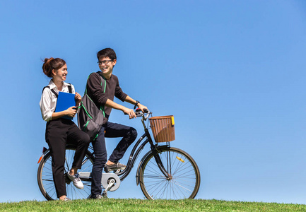 快乐和微笑年轻夫妇亚洲学生骑自行车与书在大学的户外公园与自然晴朗的蓝天背景, 在教育的概念, 放松, 爱, 体育, 健康, 生活