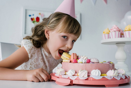 微笑的小孩子在锥体吃生日蛋糕和看照相机照片
