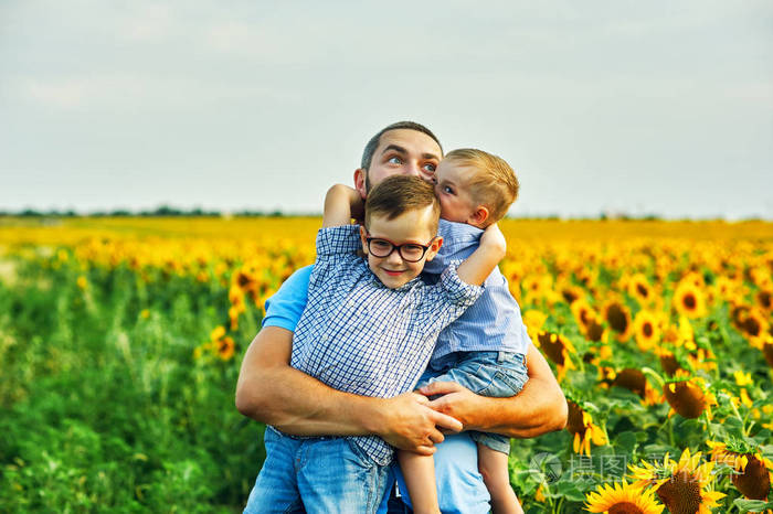快乐的父亲抱着他的两个儿子在夏天散步