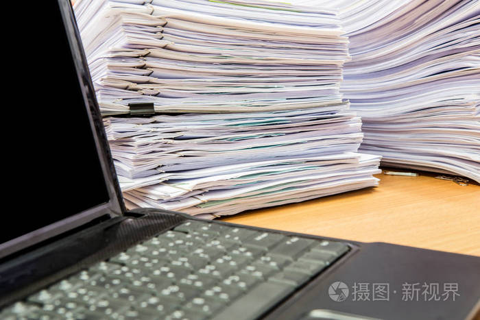 笔记本电脑和桌上的文件堆高等待管理