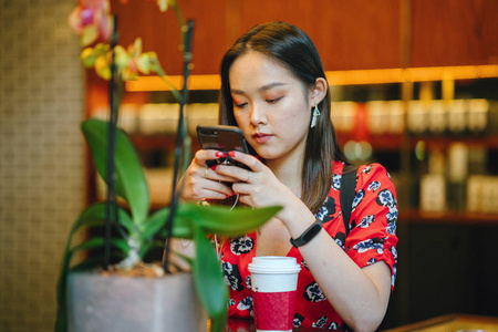 红色礼服的年轻妇女用智能手机杯咖啡