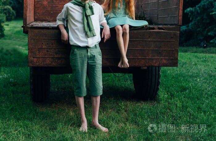 一个穿着绿色连衣裙的赤脚女孩坐在一辆旧大篷车里, 在她身旁, 赤脚