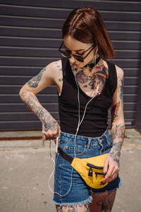 时尚纹身女孩听音乐在耳机和把智能手机口袋里