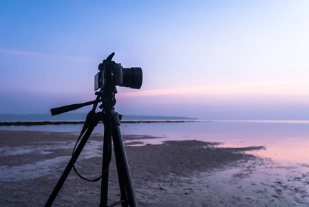 单反数码相机站在三脚架上拍摄海暮天和云景。摄影师拍摄的日出的视频在低潮的早晨