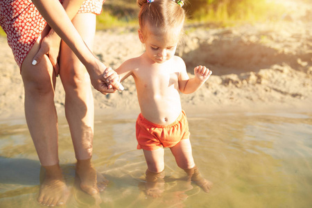 一个年轻的无法辨认的母亲抱着一个学习游泳的小女婴。暑假家庭假期的概念。与家人一起度假