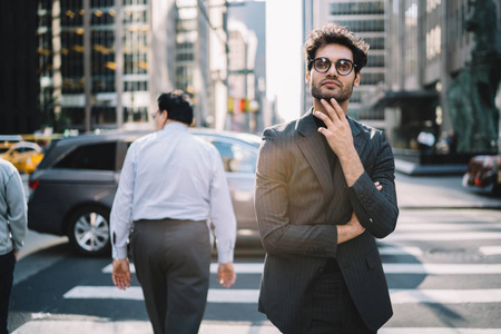 年轻英俊的男性企业家在时髦的正式穿戴在曼哈顿站在人行横道大街上的办公室, 繁华的沉思商人身着西装思考的道路上的想法