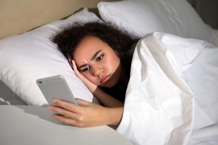困倦的女孩,用手机在床上照片