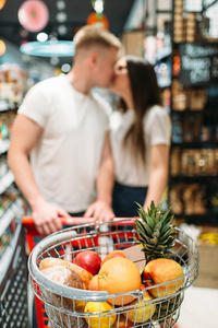 年轻夫妇在超市里亲吻着一辆手推车。食品店客户