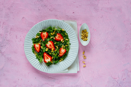 新鲜草莓沙拉盘子平躺着。芝麻草莓松树坚果和微绿色沙拉在粉红色复制空间背景。顶部视图。超级食品和排毒概念