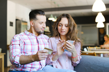 年轻漂亮的女人和男人使用智能手机和借记卡在咖啡馆
