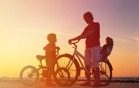 骑自行车的人家庭剪影，骑自行车在日落时的两个孩子的父亲
