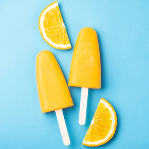 橙色的冰棒和果汁在蓝色的背景。冰 pop, 平躺, 顶部视图