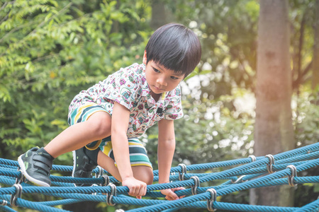 亚洲男孩正在操场上爬绳索桥图片