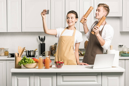 年轻夫妇采取自拍与智能手机在厨房烹饪