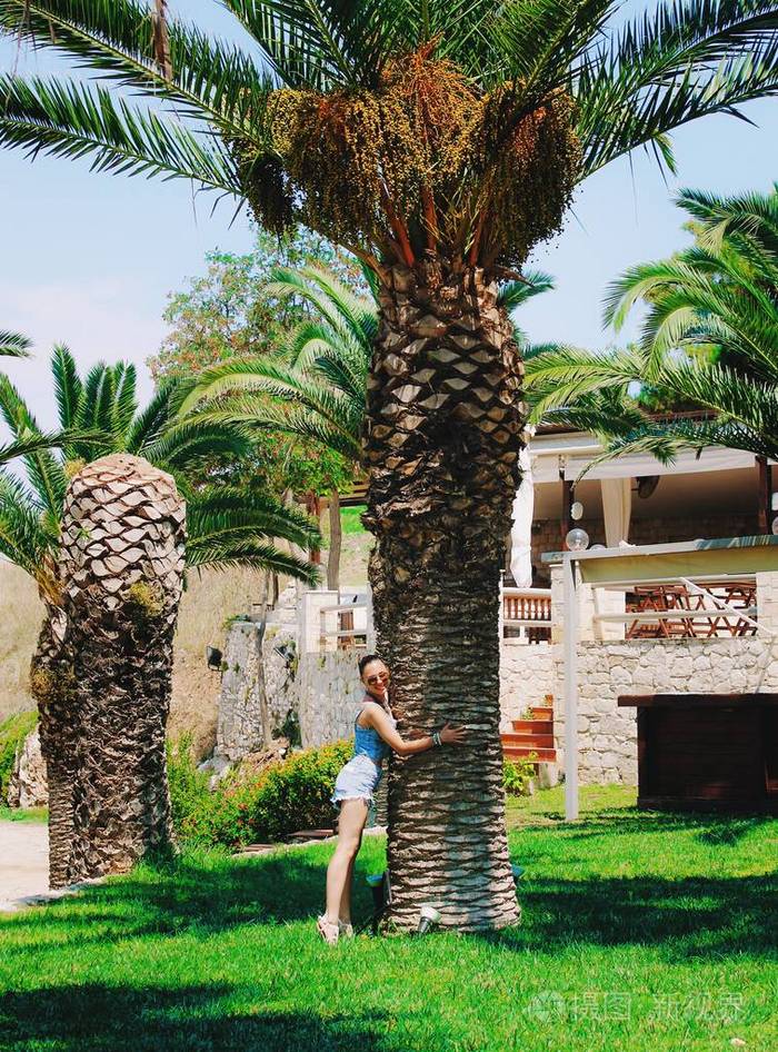 年轻漂亮的女人或希腊少女拥抱棕榈树。休假时间