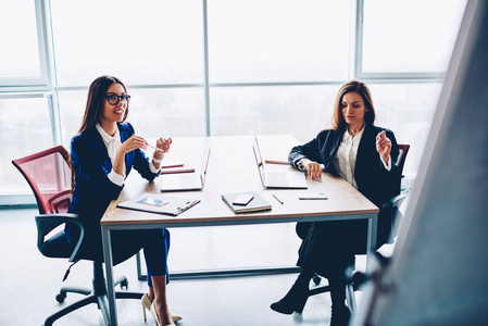 专业女性同事在典雅的正式装备讨论合作的想法在办公室, 熟练的企业妇女伙伴计划协作和财务预算在会议桌上