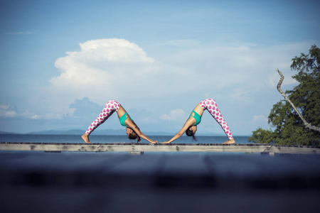 两个女人在沙滩码头上玩瑜伽姿势